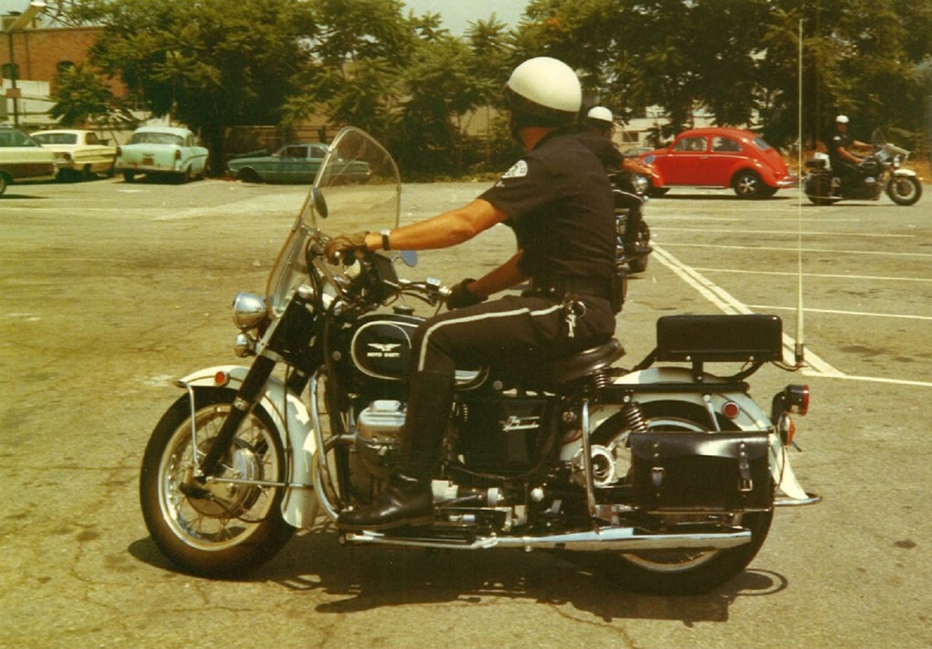 Un agente de la policía de Los Ángeles en una Moto Guzzi Eldorado 850 blanca y negra en un aparcamiento de los años 70