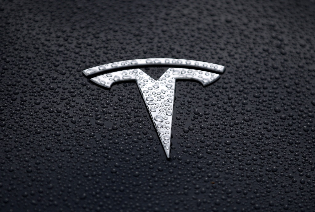Un logotipo plateado de Tesla sobre un Tesla negro bajo la lluvia en California