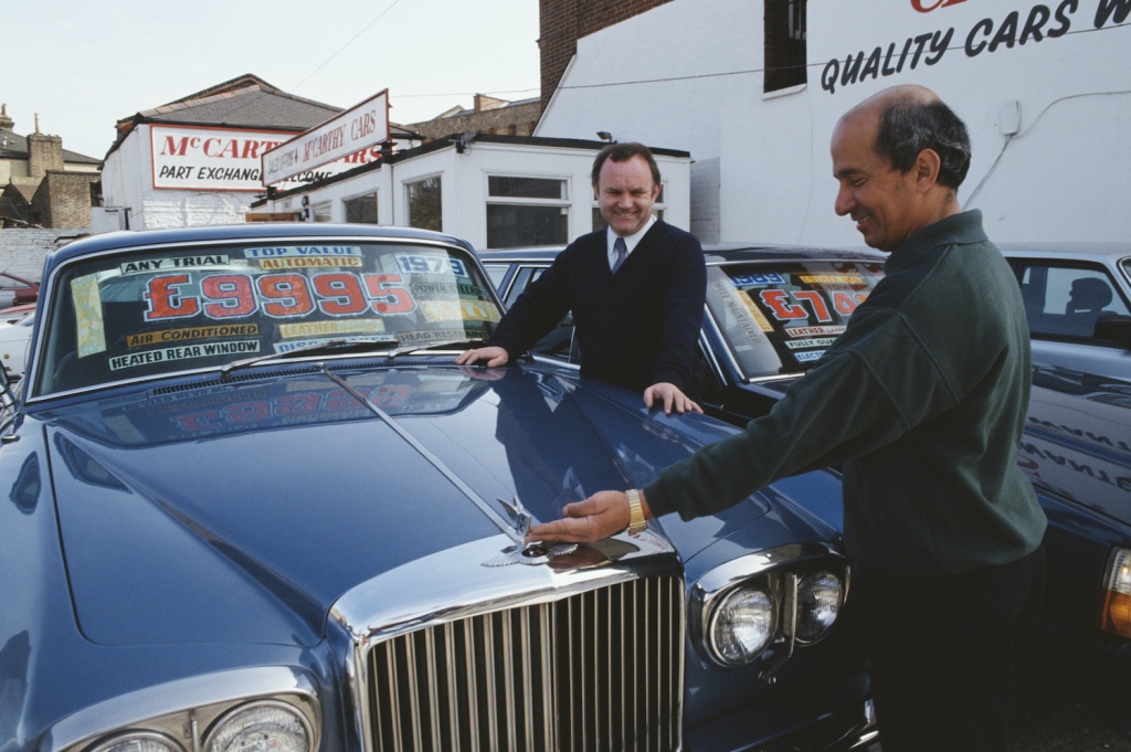 El vendedor de coches usados Vincent McCann admira un Bentley de 1979 con un cliente, Reino Unido, 1992. (Foto de Tom Stoddart Archive/Getty Images) ¿Las llamadas a revisión abiertas cambian el valor de intercambio de un coche?