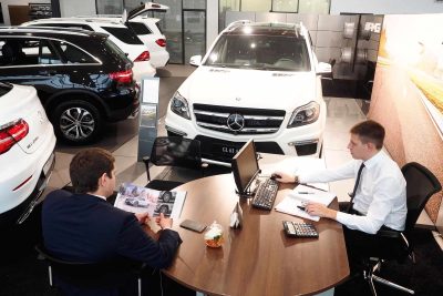 A car sales man sits with a customer at a dealership.